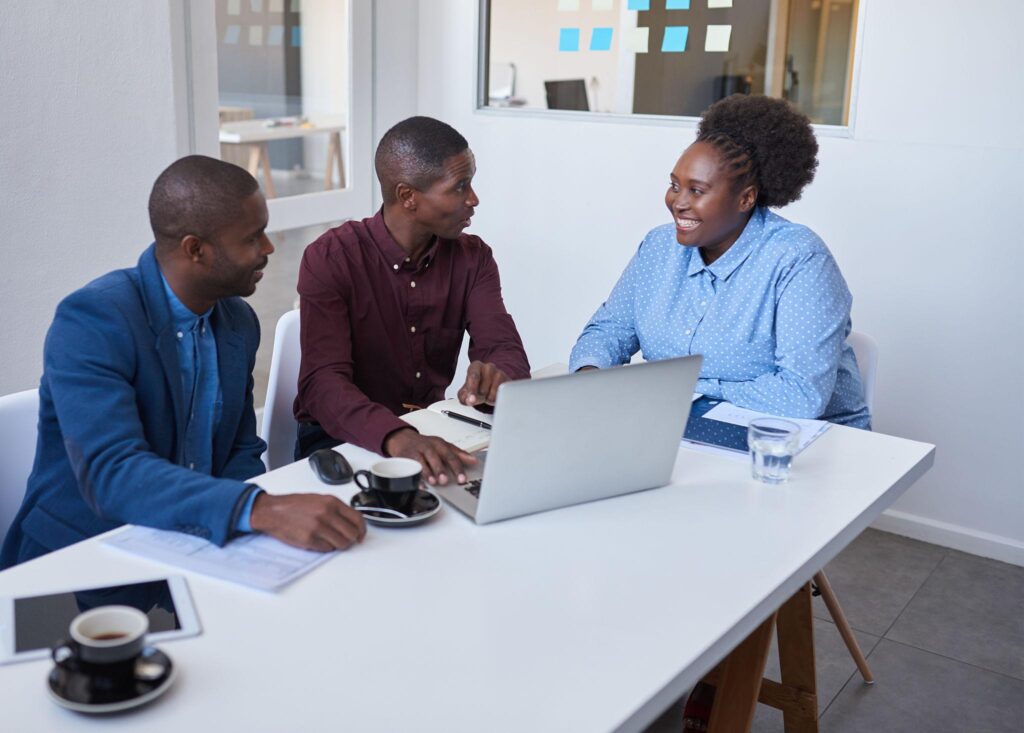 Three African professionals discussing strategy around a laptop during a consultancy session.